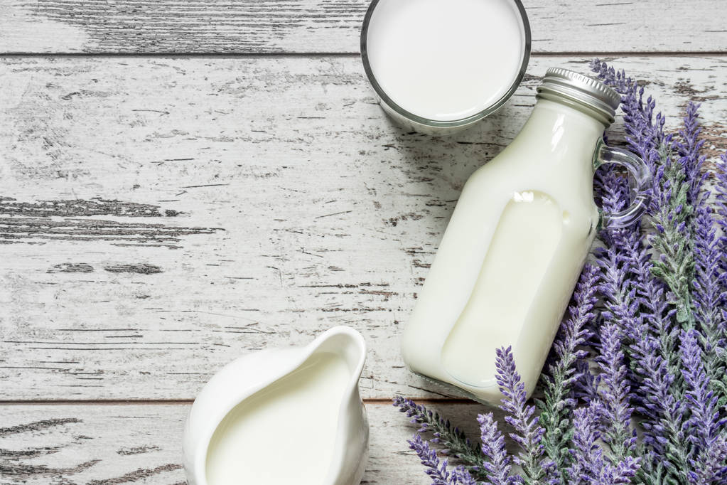 Vintage glazen flesje met melk, een glas met melk en een prachtige witte kruik naast een tak van lavendel op een vintage houten achtergrond. Van bovenaf bekijken. - Foto, afbeelding
