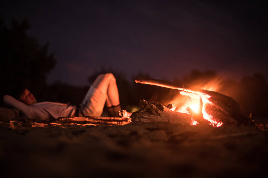 Hombre haciendo camping y acostado en la playa cerca del fuego por la noche
 - Foto, imagen