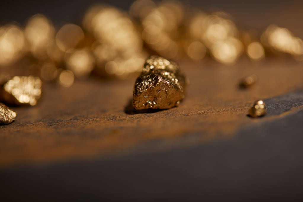 selective focus of golden stones on grey and brown marble surface with blurred background - Photo, Image