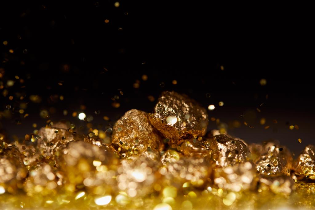 Selektiver Fokus von goldenen Steinen auf glitzernder Oberfläche und schwarzem Hintergrund - Foto, Bild