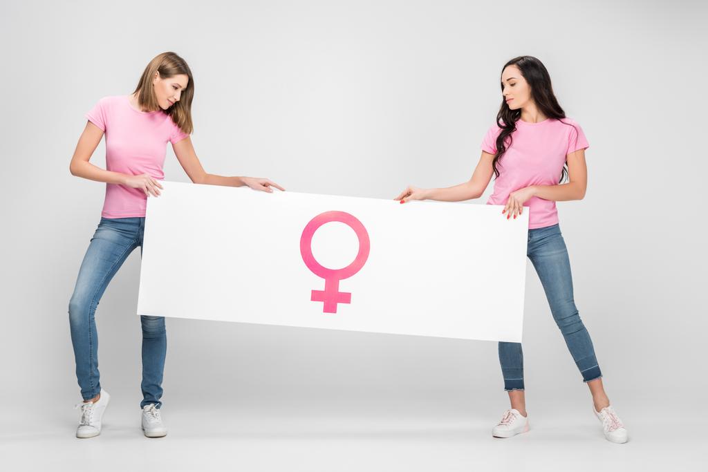 ελκυστικές γυναίκες κατέχουν μεγάλη πινακίδα με θηλυκό σύμβολο σε γκρι φόντο - Φωτογραφία, εικόνα