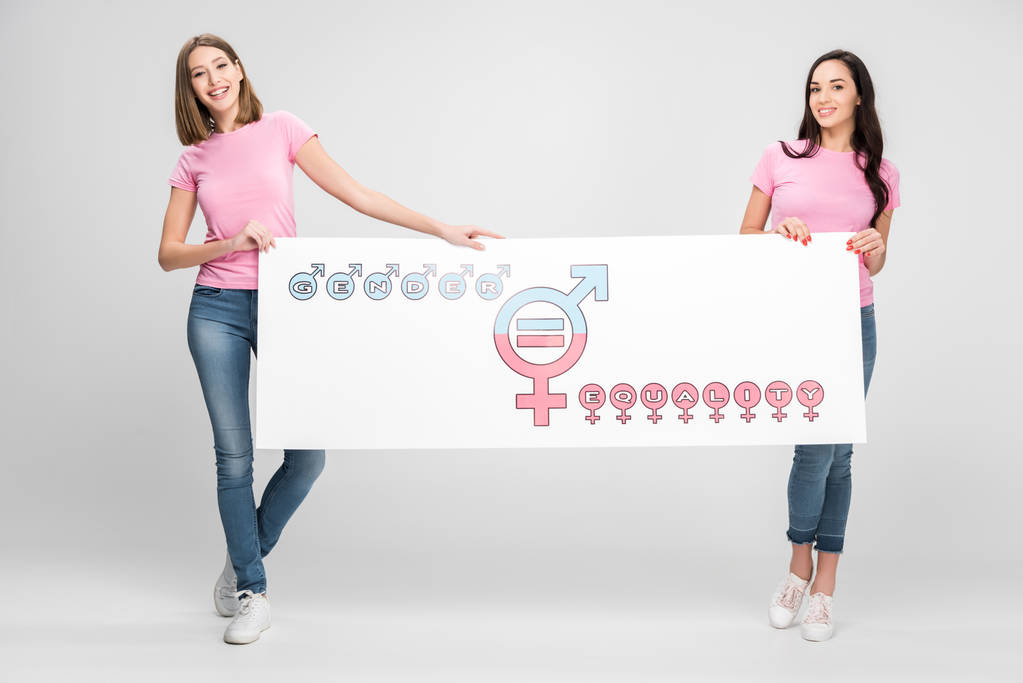 χαρούμενα γυναίκες κατέχουν μεγάλη πινακίδα με το σύμβολο ισότητας των φύλων σε γκρίζο φόντο - Φωτογραφία, εικόνα