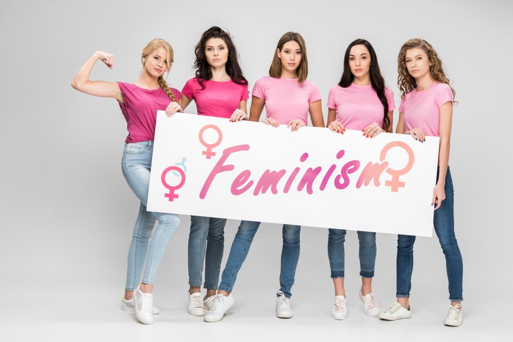 σοβαρά κορίτσια που κατέχουν μεγάλη πινακίδα με την επιγραφή του φεμινισμού σε γκρίζο φόντο - Φωτογραφία, εικόνα