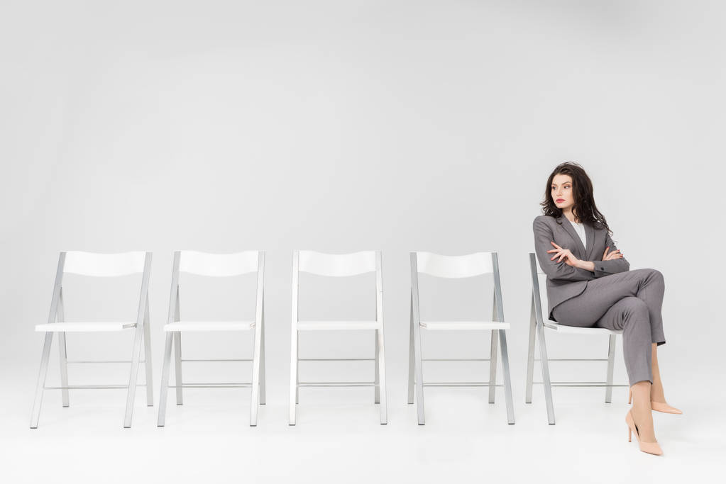 donna sicura seduta con braccia incrociate e gambe incrociate sulla sedia isolata su grigio
 - Foto, immagini