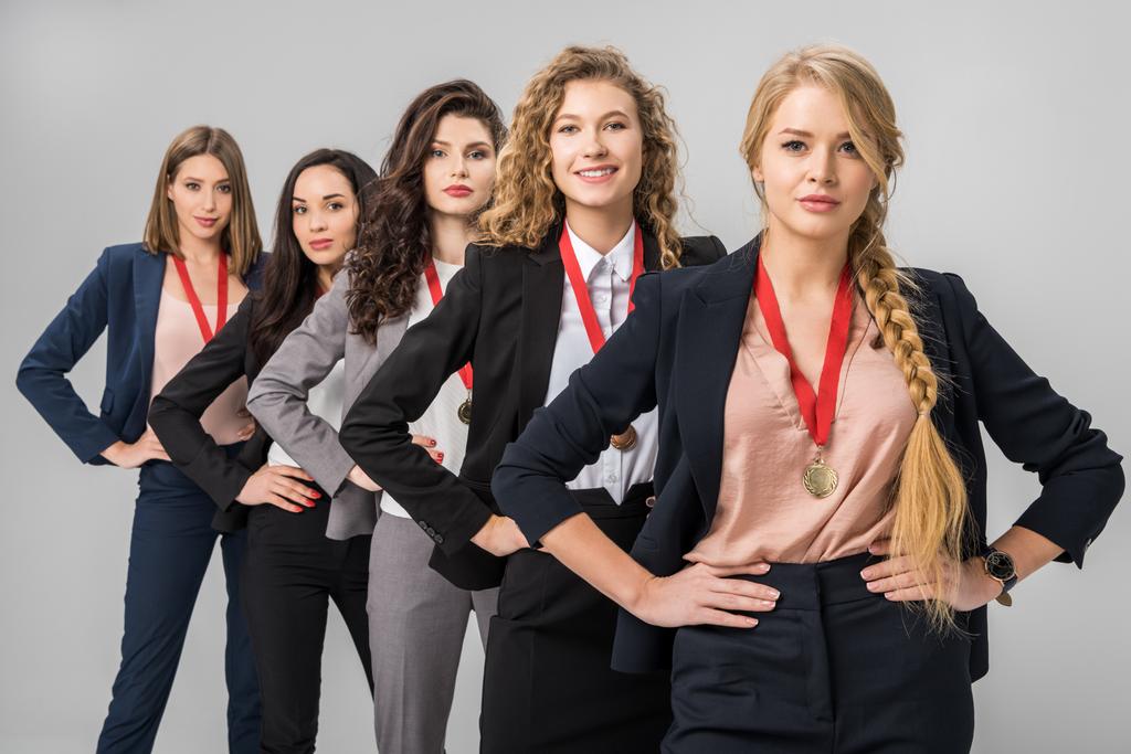 Selektiver Fokus schöner Geschäftsfrauen, die mit Medaillen in grau vereinzelt stehen  - Foto, Bild