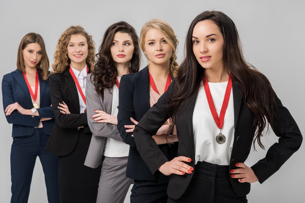 selectieve aandacht van aantrekkelijke jonge vrouwelijke ondernemers permanent met medailles geïsoleerd op grijs  - Foto, afbeelding