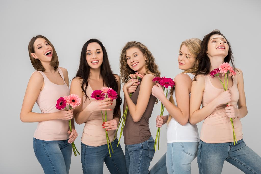 vrolijke meisjes houden van roze bloemen en glimlachend geïsoleerd op grijs - Foto, afbeelding