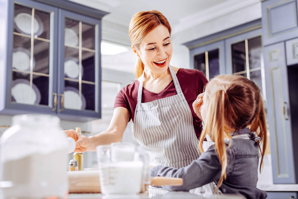 Mujer emocionada mirando a su hija y sonriendo mientras cocinaba con ella
 - Foto, imagen