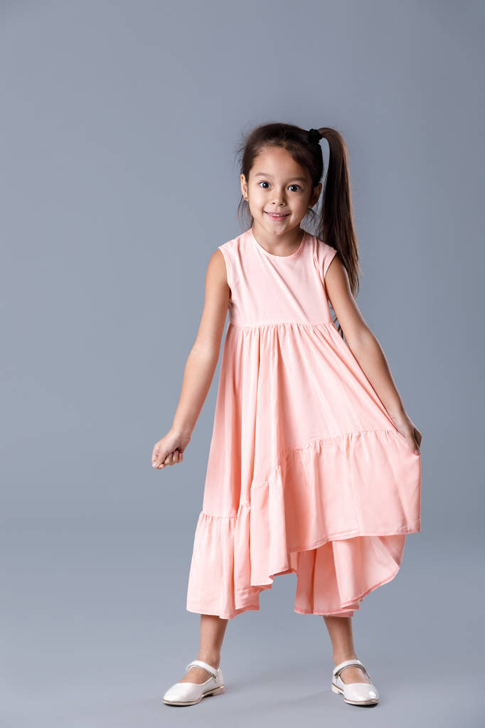 klein meisje in roze jurk poseren op grijze achtergrond. - Foto, afbeelding