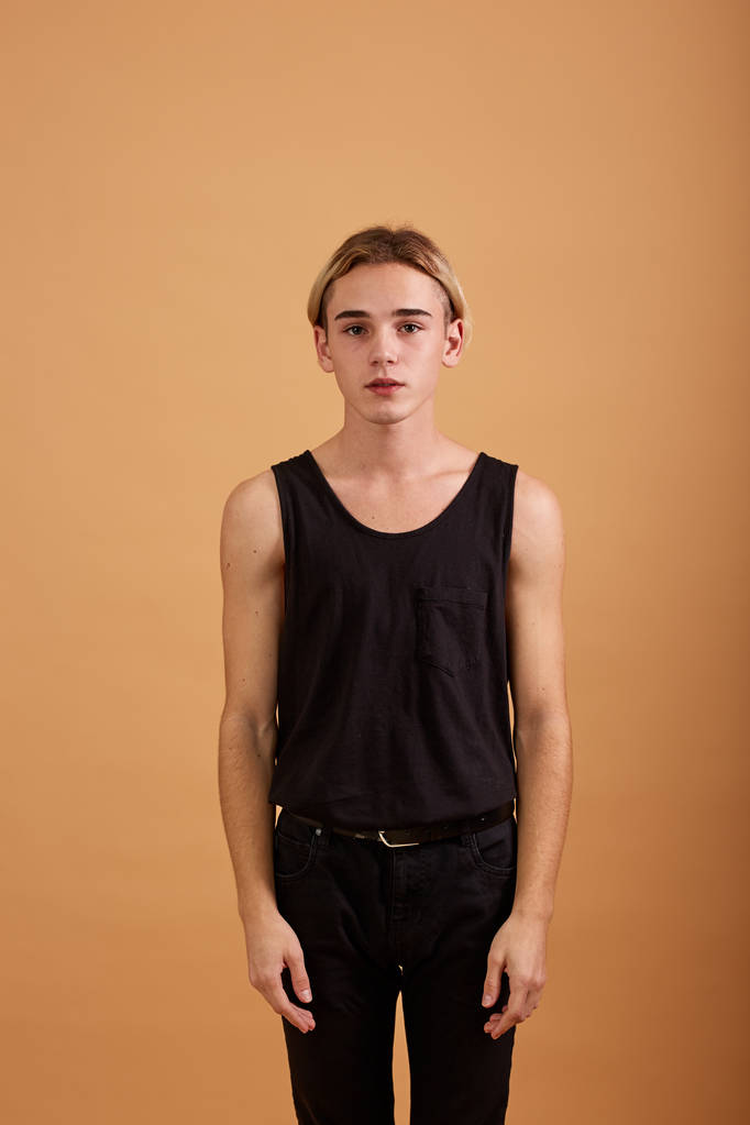 Fiatal szőke srác öltözött egy fekete pólót és a nadrágot, pózol a stúdióban, a bézs háttér - Fotó, kép