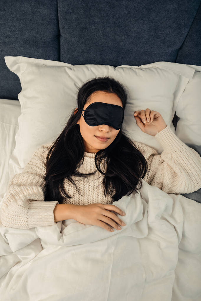Asian woman wearing black sleeping mask lying in bed - Photo, Image