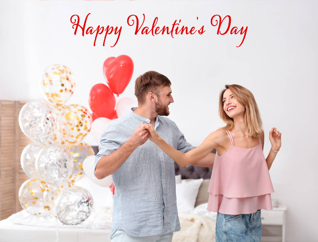 Jong koppel dansen in slaapkamer ingericht met lucht ballonnen en de tekst Happy Valentine's Day - Foto, afbeelding