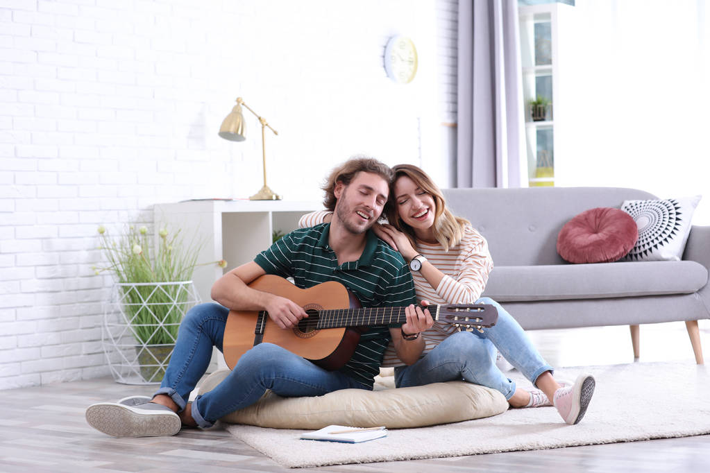 Jonge man spelen gitaar voor zijn vriendin in woonkamer - Foto, afbeelding