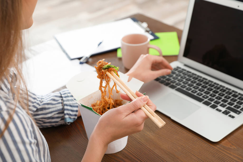 Офісний працівник використовує ноутбук, маючи локшину на обід на робочому місці, крупним планом. Доставка їжі
 - Фото, зображення