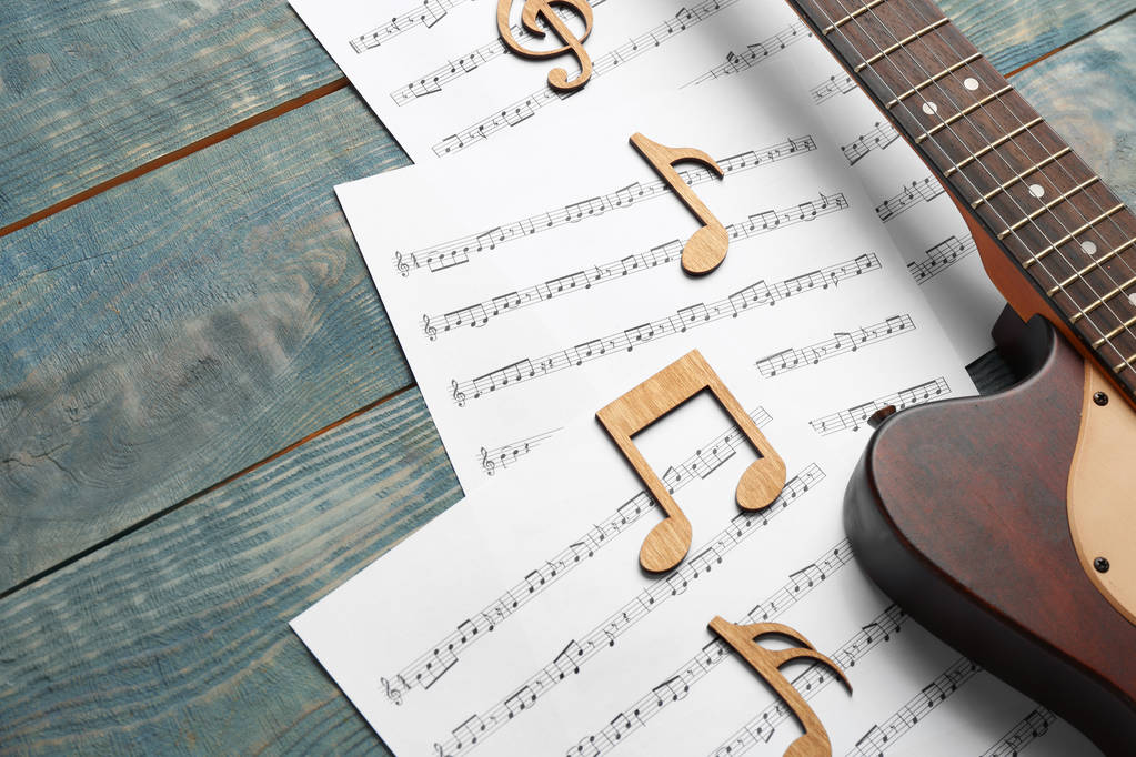 Гітара та листи з музичними нотами на дерев'яному столі. Простір для тексту
 - Фото, зображення