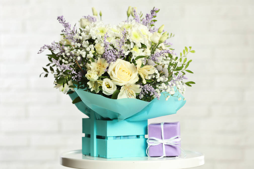 Beautiful bouquet of flowers in decorative crate and gift box on table against light background - Photo, Image