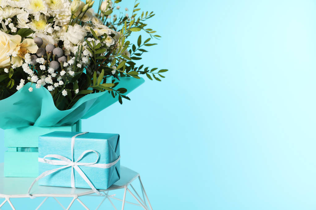 Beautiful bouquet of flowers and gift box on table against color background. Space for text - Photo, Image