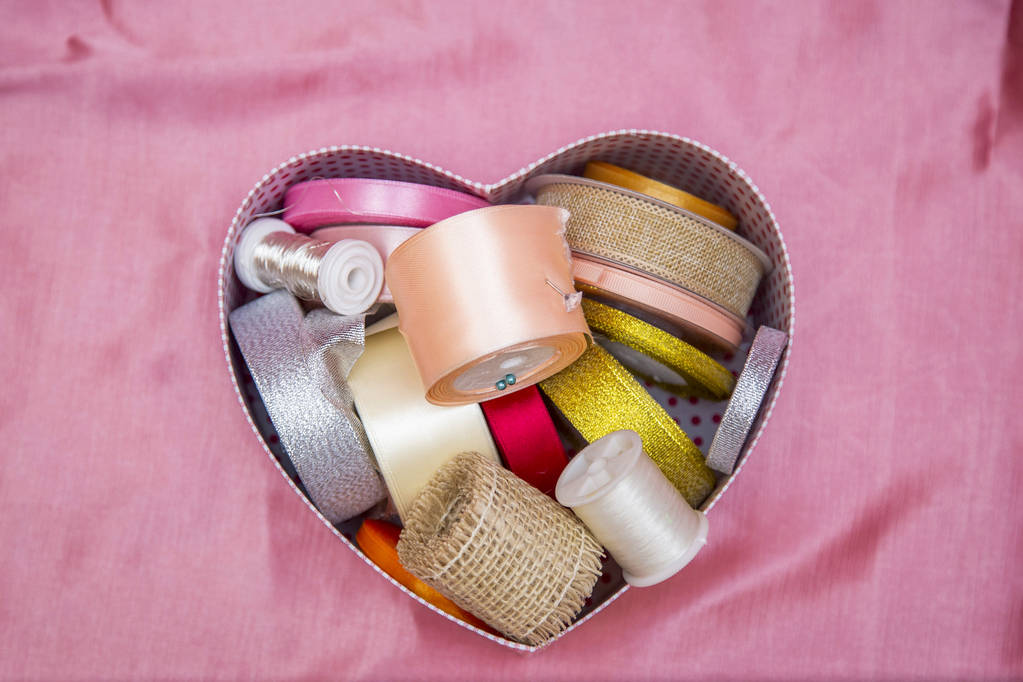 Feld in Form eines Herzens mit Knäueln aus bunten Bändern für Handarbeit auf rosa Hintergrund - Foto, Bild