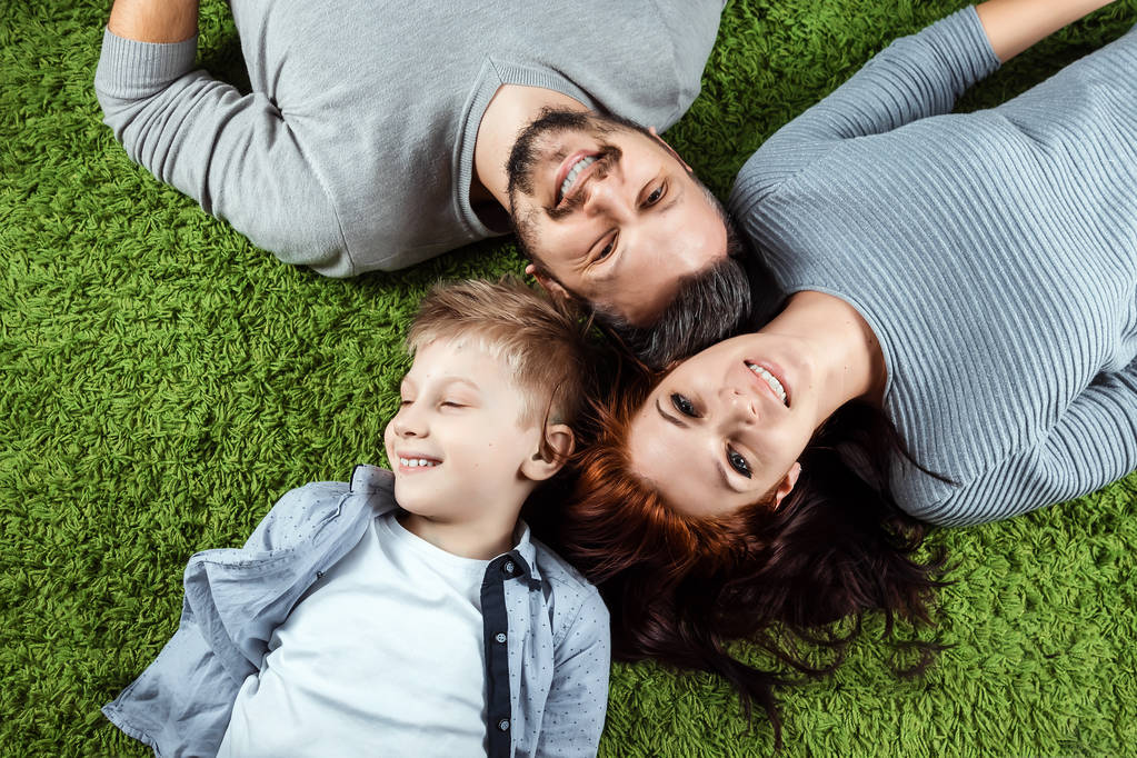 Bovenaanzicht, gelukkige familie, moeder van de vader en zoon zijn lachende liggend op een groen tapijt. Het concept van de familie relaties, familie, geluk, vreugde. - Foto, afbeelding