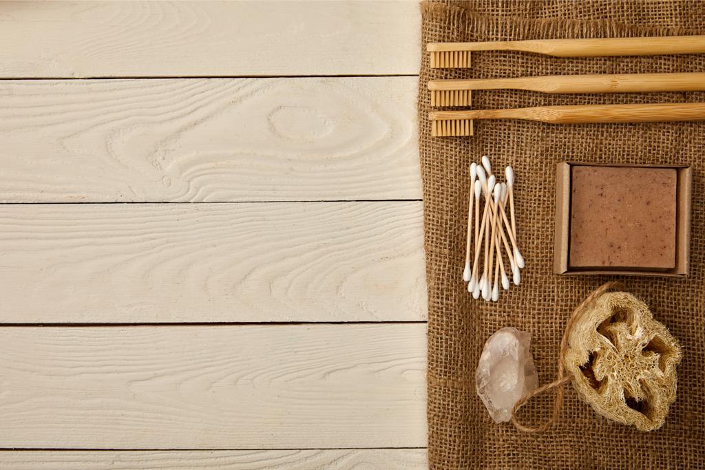 flat lay of various hygiene and care items arranged on sackcloth on white wooden surface, zero waste concept - Photo, Image