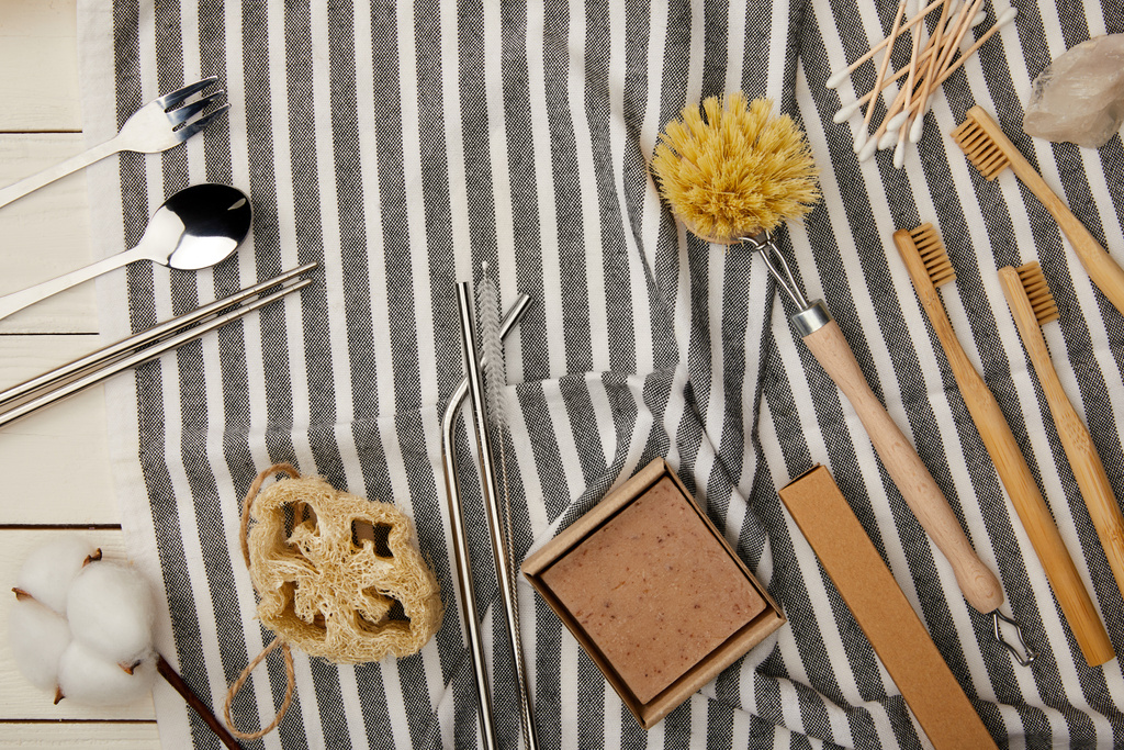 top view of cutlery, hygiene and care items on striped towel on white wooden surface, zero waste concept - Photo, Image