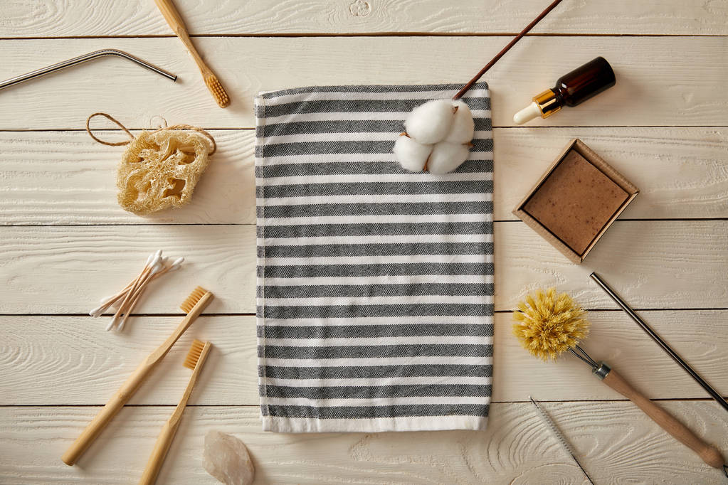bovenaanzicht van verschillende hygiënische zorg artikelen en gestreepte handdoek op witte houten oppervlak, nul afval concept - Foto, afbeelding