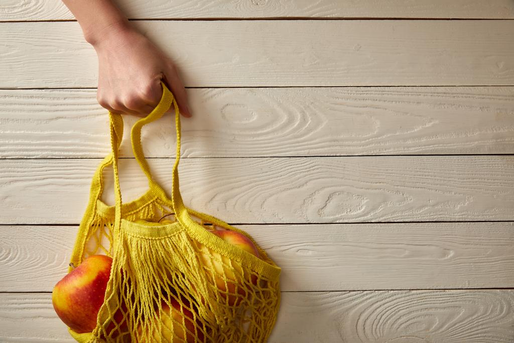 περικοπεί προβολή γυναικείο χέρι με κορδόνι τσάντα γεμάτη μήλα βιασμό σε λευκή ξύλινη επιφάνεια, μηδενικών αποβλήτων έννοια - Φωτογραφία, εικόνα