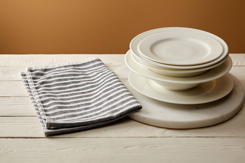 стек з білих тарілок і смугастий бавовняний рушник на білій дерев'яній поверхні
 - Фото, зображення