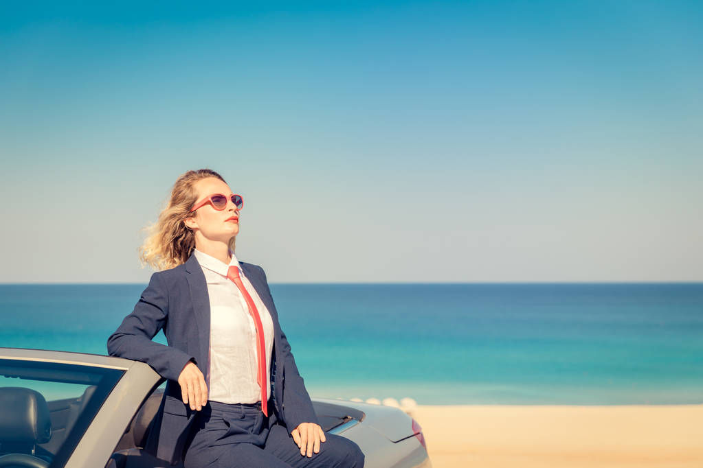 Successful young businesswoman on the beach. Woman sitting on the cabriolet classic car. Summer vacations and freedom travel concept - Photo, Image