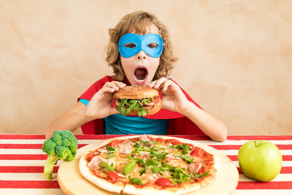 Supersankarilapsi syö superruokaa. Onnellinen lapsi lounaalla kotona. Terveellisen syömisen ja elämäntavan käsite. Vihreä kasvisruoka
 - Valokuva, kuva