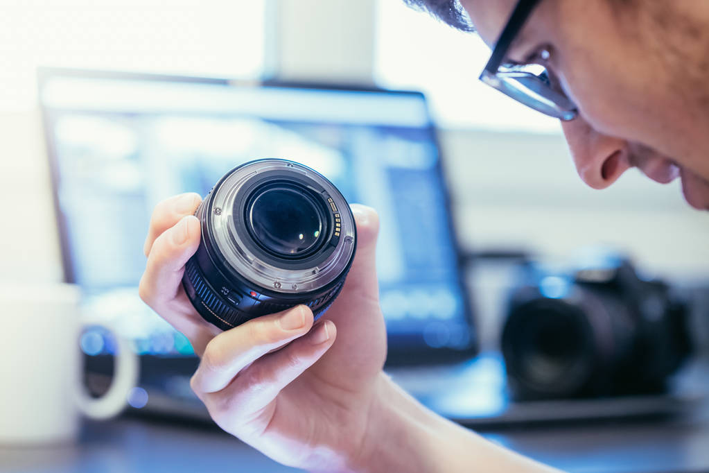 Genç fotoğrafçı bir fotoğraf lens, dizüstü bulanık arka planda bakıyor - Fotoğraf, Görsel