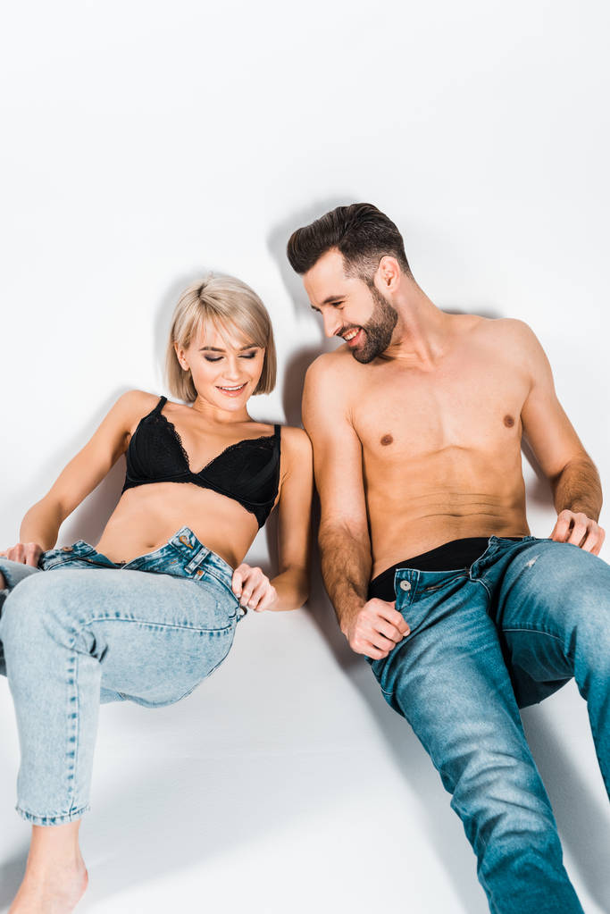 sexy shirtless man en aantrekkelijke vrouw opstijgen jeans op grijs - Foto, afbeelding