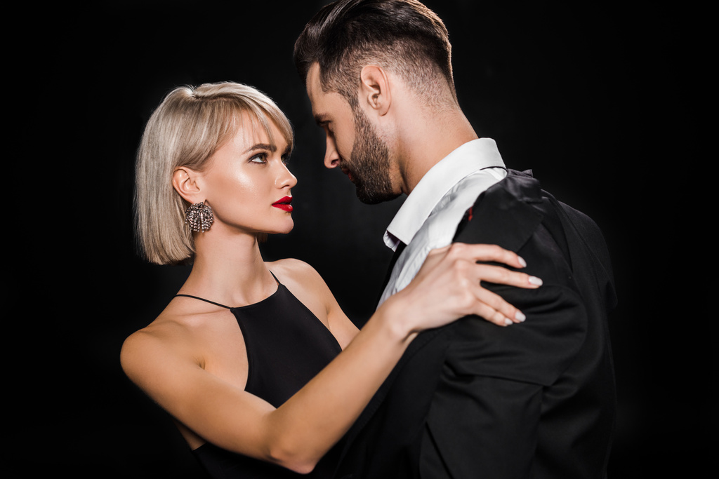 passionate blonde woman undressing handsome man isolated on black - Photo, Image
