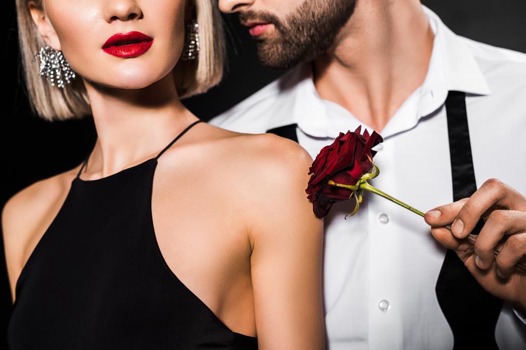cropped view of man touching womans shoulder with rose flower, isolated on black - Photo, Image