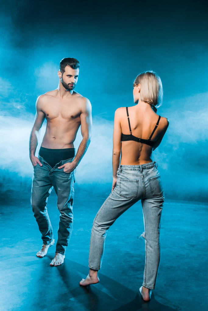 beautiful couple in jeans and underwear posing on blue smoky background - Photo, Image