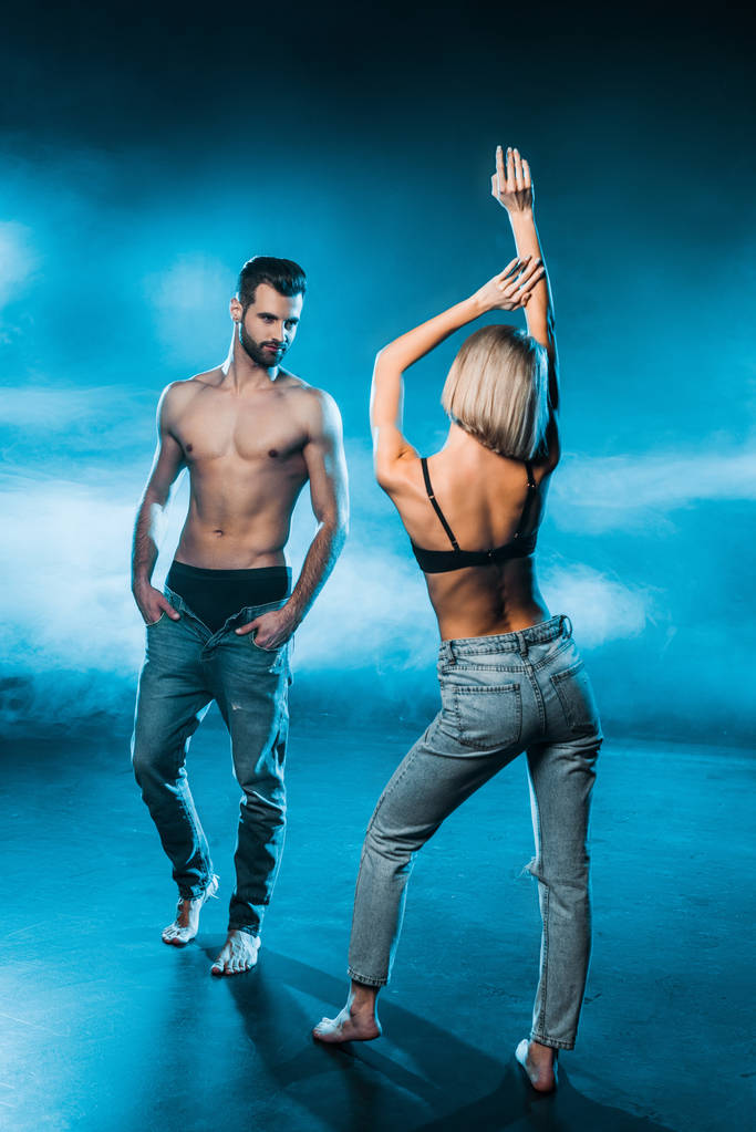 Sinnliches Paar in Jeans und Unterwäsche posiert auf blauem rauchigen Hintergrund - Foto, Bild