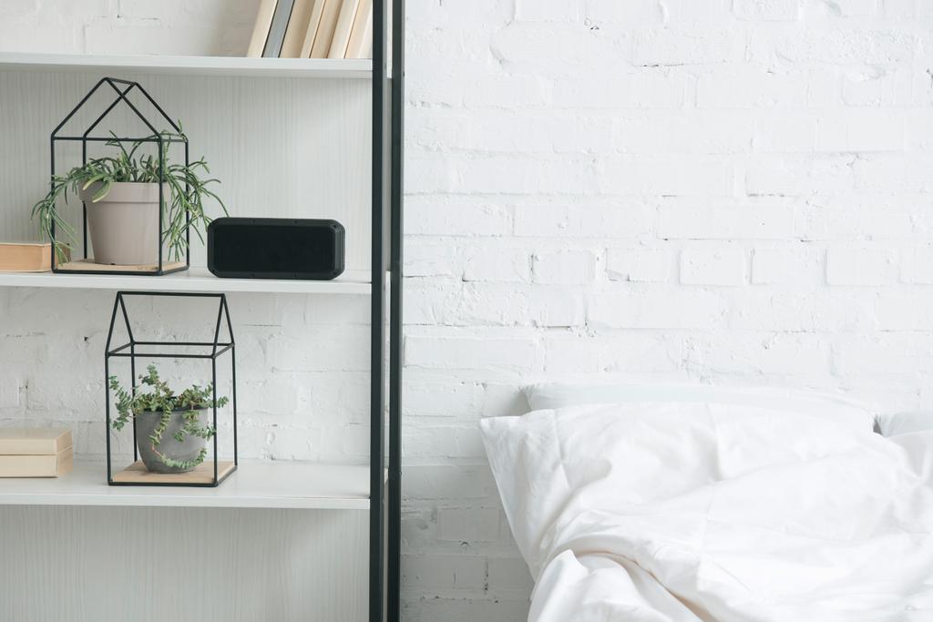 ράφι με φυτά, ξυπνητήρι και λευκό κρεβάτι  - Φωτογραφία, εικόνα