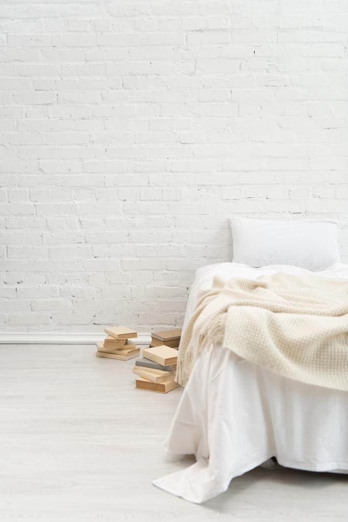 dormitorio con almohada en cama vacía y libros en el suelo
 - Foto, Imagen