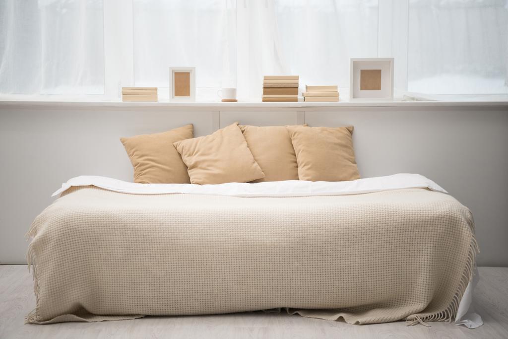 Interior do quarto com almofadas marrons na cama, livros, xícara de café e molduras para fotos
  - Foto, Imagem