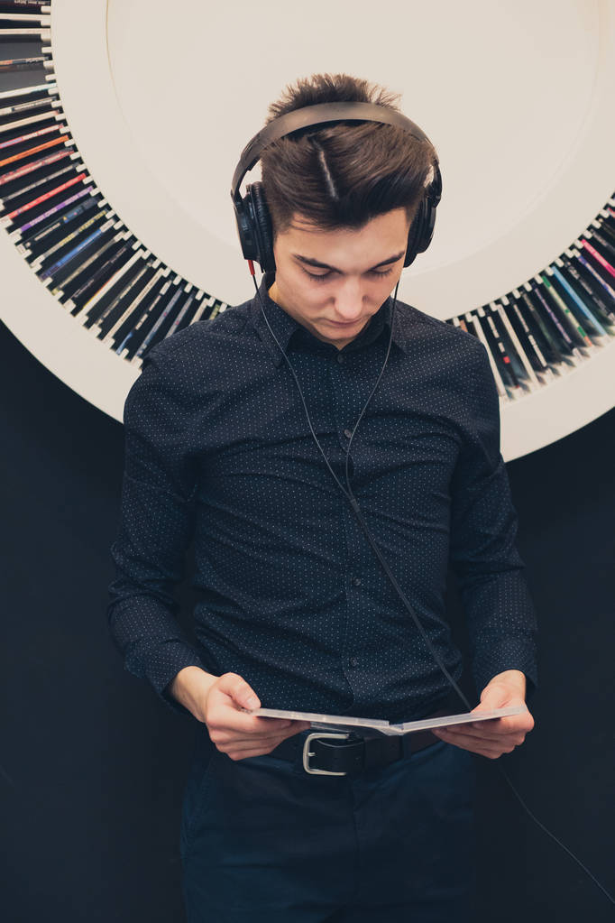 Hallgató-hoz zene keresztül fejhallgató könyvespolc felvételek mellett álló fiatalember - Fotó, kép