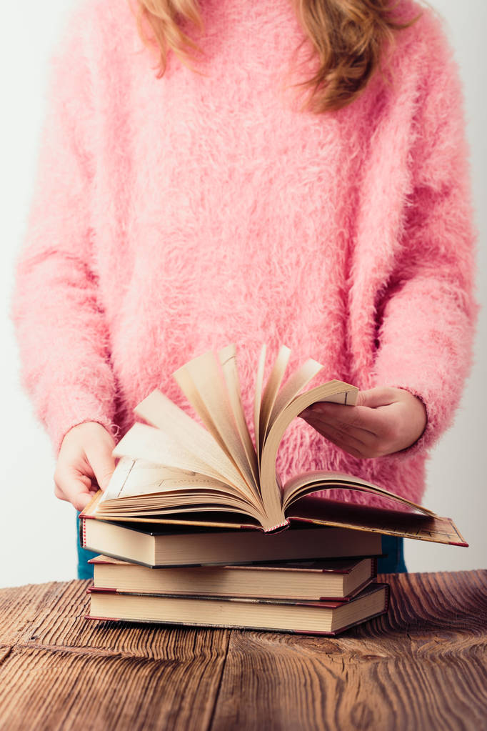 Młoda dziewczyna przewracanie stron książki w bibliotece kilka książek na drewnianym stole. Nastolatek dziewczyna ubrana w różowy sweter i dżinsy. Pionowe zdjęcie - Zdjęcie, obraz
