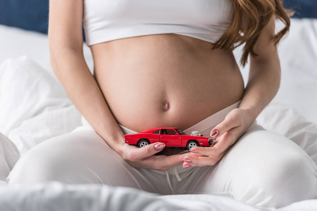 Oříznutý pohled těhotné ženy držící červené autíčko - Fotografie, Obrázek