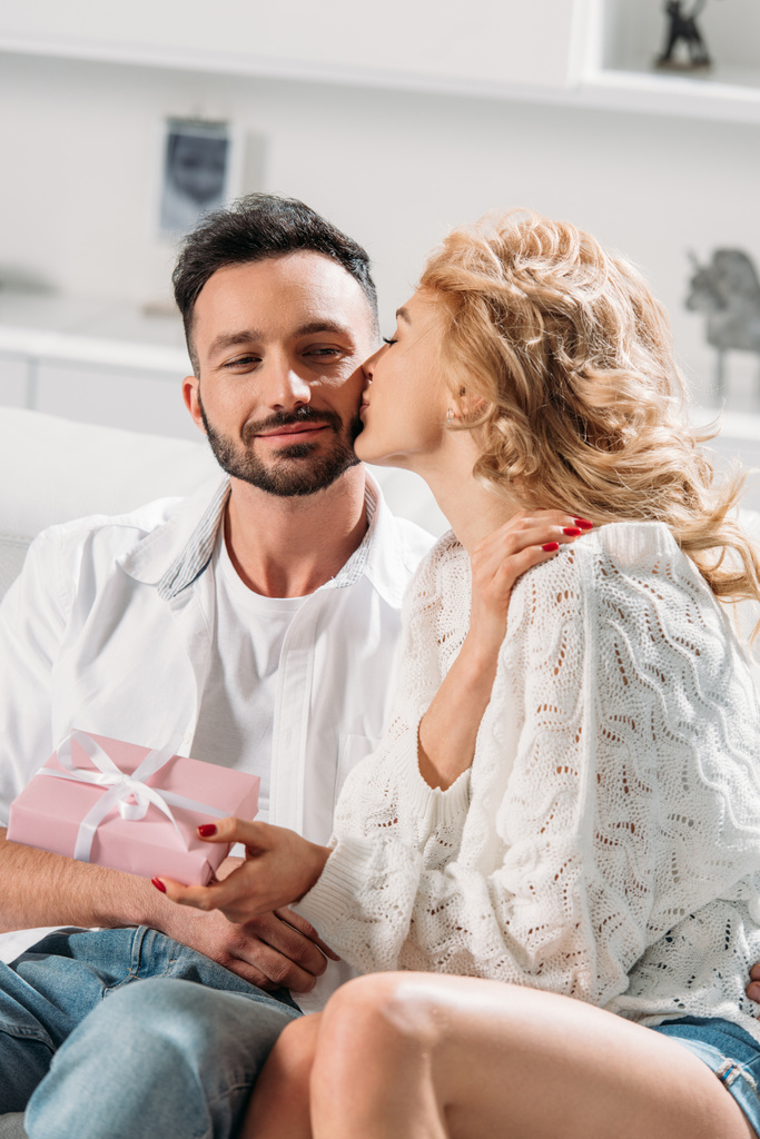 Chica rubia sosteniendo presente caja y besar novio en la mejilla
 - Foto, imagen