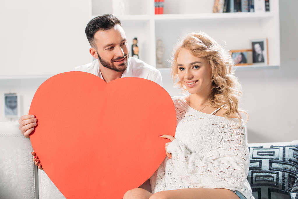 Feliz pareja romántica sonriendo mientras sostiene el corazón rojo
  - Foto, imagen