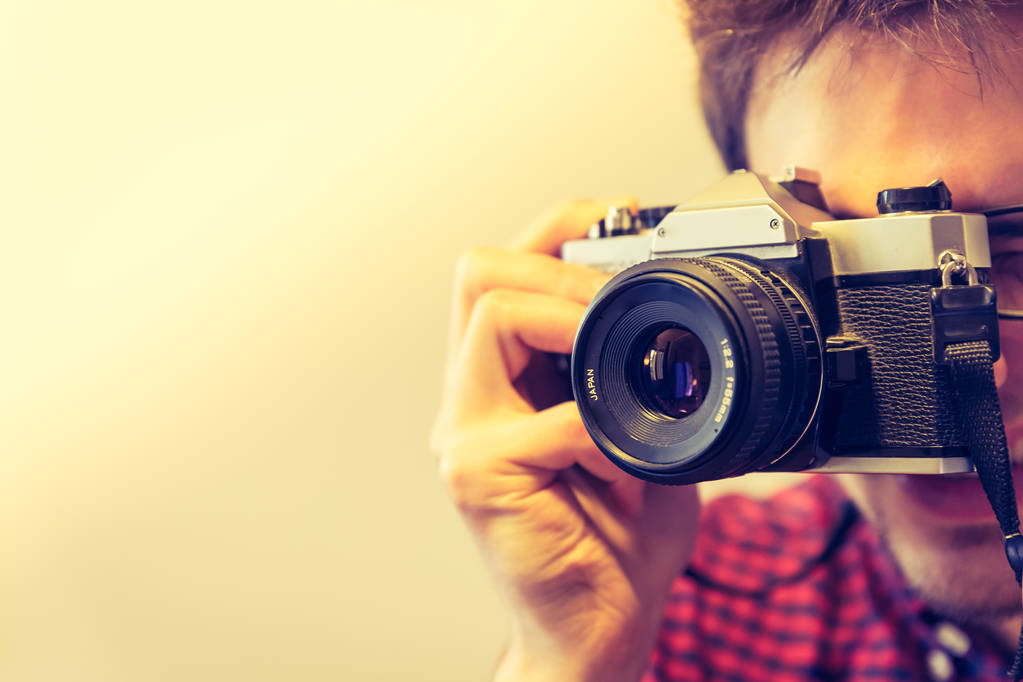 Jovem de camisa vermelha-azul verificado está tirando uma foto com uma câmera vintage, estilo retro
 - Foto, Imagem