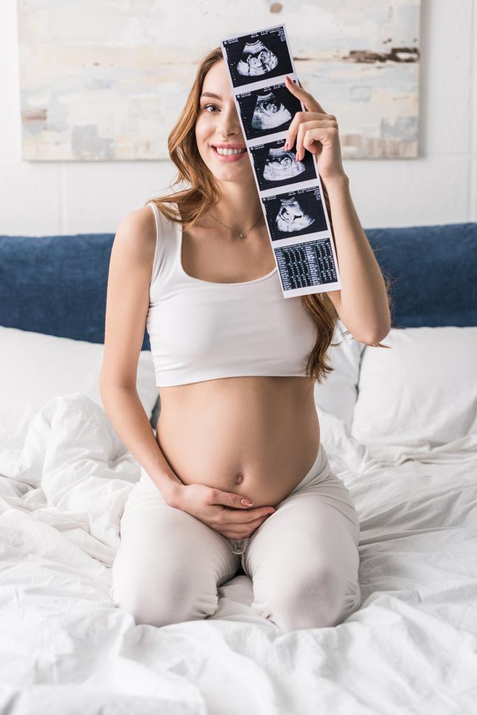 Mujer embarazada emocionada sentada en la cama con ecografías
 - Foto, imagen