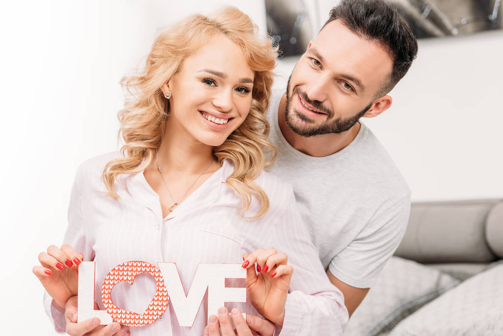 Smiling romantic couple holding word love and looking at camera - Photo, Image