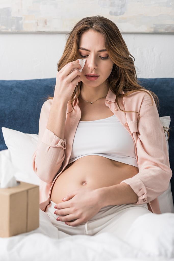 Szomorú terhes nő ült az ágyban, és törölgette az arcát szalvéta - Fotó, kép