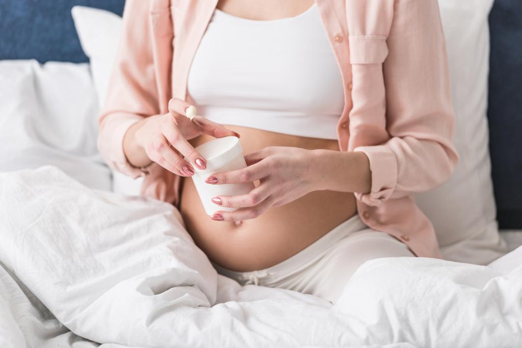 Vista parcial da mulher grávida recipiente de abertura com creme
 - Foto, Imagem