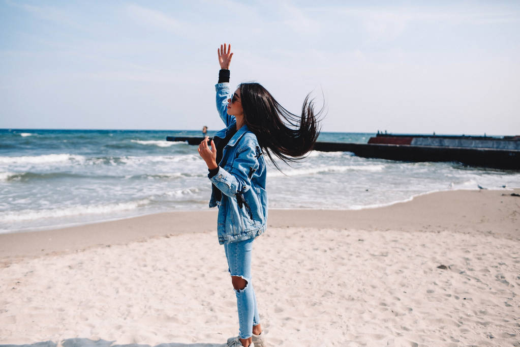 Женщина отдыхает на пляже, наслаждаясь летней свободой с распростертыми объятиями и волосами на ветру на берегу моря. Смешанная раса Азиатская кавказская девушка на летних каникулах отпуск вне
 - Фото, изображение